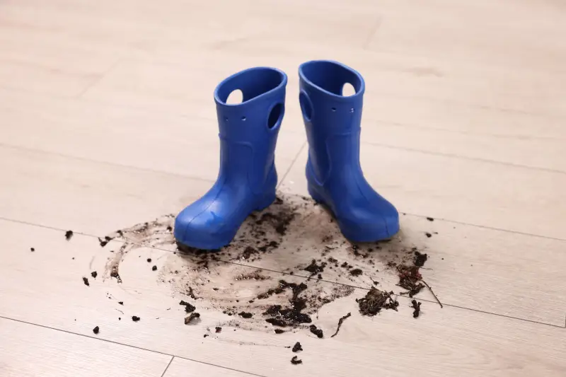 Rubber boots with mud on wooden floor